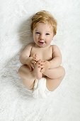 Toddler lying on blanket, holding feet, smiling