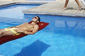 Man Relaxing in Pool While Woman Walks by Pool Deck