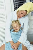 Mother sitting behind daughter in bathroom, girl wrapped in a towel