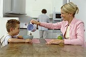 Mother and son sitting at table in kitchen, mother pouring milk in bowl