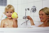 Mother and daughter sitting in bathtub, girl showing rubber duck