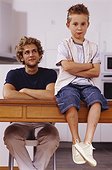 Father and son sitting in kitchen with arms crossed