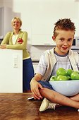 Son sitting on table in kitchen, mother standing in the back