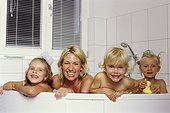 Mother and her three daughters looking over rim of bathtub in camera