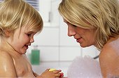 Mother and daughter sitting in bathtub, looking at soap