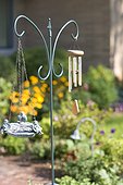 A wind chime and a carved object is hung on a stand in the garden