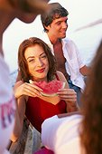 Young woman eating a water melon, young man behind her