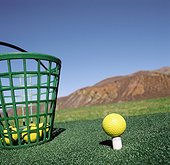 Golf ball on a tee and a basket of golf balls