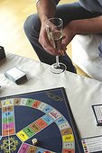Man holding a Champagne Glass and a Board Game laying on a Table (cropped)