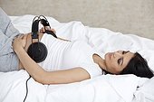 Pregnant woman lying in bed with headphones on belly