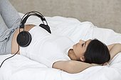 Pregnant woman lying in bed with headphones on belly
