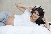 Pregnant woman lying in bed with headphones