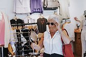Senior woman in clothes shop trying sunglasses
