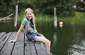 Portrait of smiling blond hair girl sitting on pier in a lake