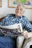 Elderly man reading newspaper while sitting in living room