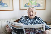 Senior adult man reading newspaper in living room