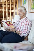 Elderly woman reading novel while sitting on sofa in living room