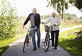 Front view of active elder couple in park walking with bicycles