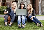 Mature female friends sitting on lawn with laptop