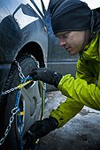 Man tying snow chain on his car's wheel