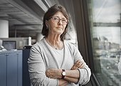 Portrait of confident senior businesswoman standing arms crossed by window in office