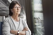 Thoughtful senior businesswoman standing arms crossed by window in office