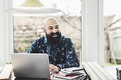 Happy male architect looking away while using laptop at home office