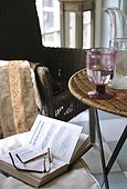 Book and eyeglasses on chair next to table with glass of water