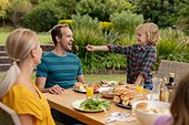 Caucasian boy feeding smiling father from his fork during family meal in garden