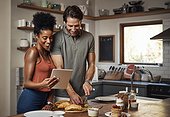 Young couple cooking healthy food together following recipes online on a tablet, step by step. Happy, cheerful and smiling husband and wife making dinner in the kitchen at home.