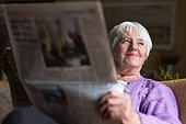 Senior woman reading morning newspaper, sitting in her favorite chair in her living room