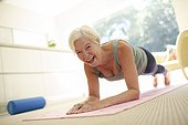 Portrait happy senior woman practicing plank pose on yoga mat at home