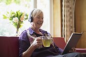 Happy senior woman with headphones and digital tablet drinking tea