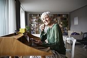 Smiling active senior woman listening music while sitting on chair at home