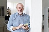 Cheerful businessman with smart phone leaning on column at home