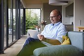 Smiling man using tablet PC sitting on sofa at home