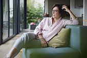 Thoughtful woman wearing eyeglasses sitting on sofa at home