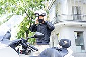 Male biker putting on helmet while standing by motor scooter