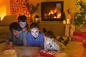Family eating popcorn and watching video on laptop in ambient Christmas living room with fireplace