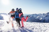 Skiers mother with teenage son and daughter kicking up on snow covered mountain top Alpe-d Huez Rhone-Alpes France