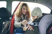 Mother fastening little girl with safety seat belt in a car