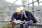 Architect and worker discussing building plan on scaffolding on a construction site