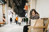 Spain, Reus, happy young woman sitting on a bench with her shopping bags