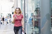 Smiling woman walking on the street with shopping bags looking at her smartphone