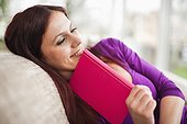 portrait of young woman lying on sofa reading book