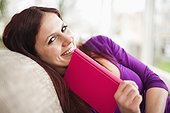 portrait of young woman lying on sofa reading book