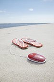 pair of flip flops and computer mouse on sandy beach