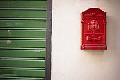 a red mailbox mounted on a white wall beside a green door; genoa liguria italy