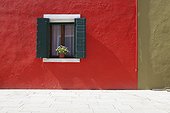 a flower pot sits in a window with shutters open in building painted bright red; burano venezia italy