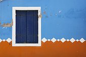 paint peeling off of a decorative exterior wall and a closed shutters on a window; burano venezia italy